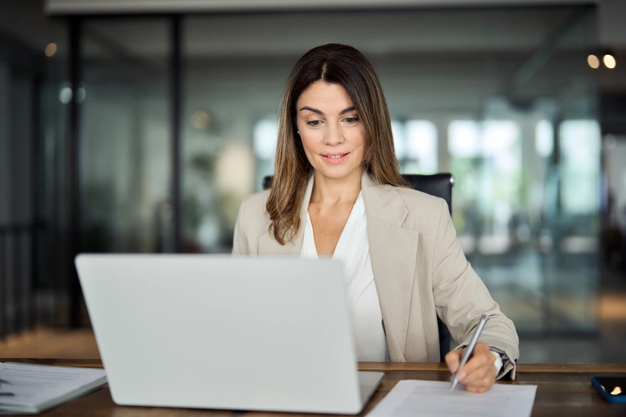 Lächelnde Frau prüft ihre Finanzen Laptop und macht Notizen